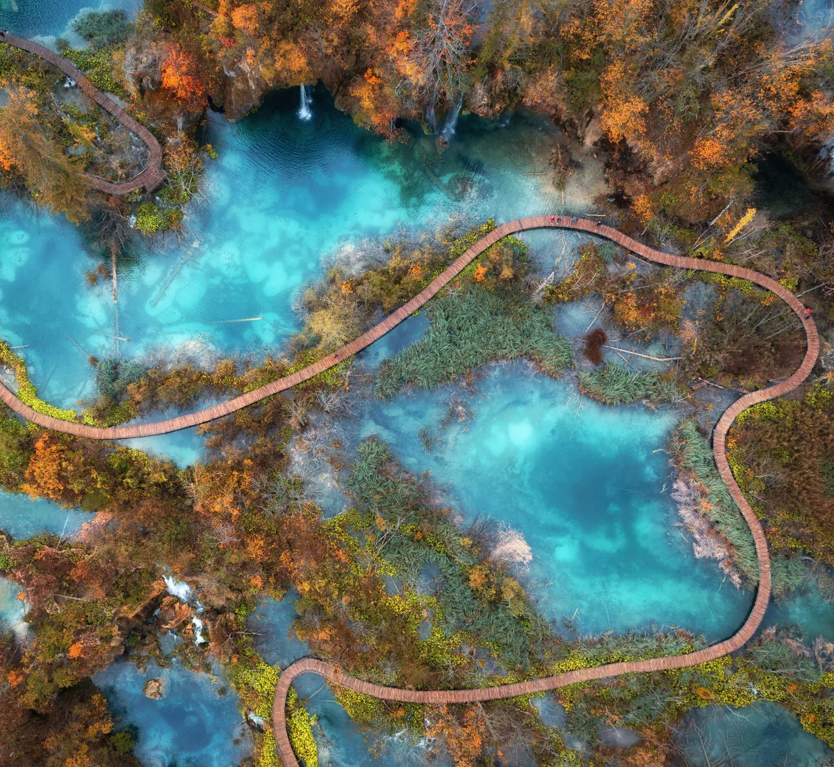 An aerial photograph of lakes and boardwalks at Plitvice: a real landscape that reads like a map of a story world, with one path threading every part of it together