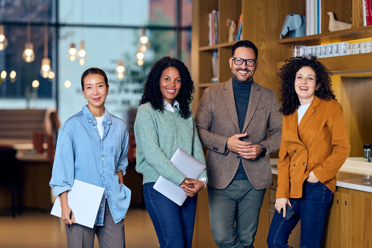 Four colleagues standing together in a studio office, notebooks in hand
